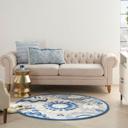 Round blue floral rug (4' round) in a bright living space with a beige tufted sofa, blue patterned cushions, and a gold pedestal side table.