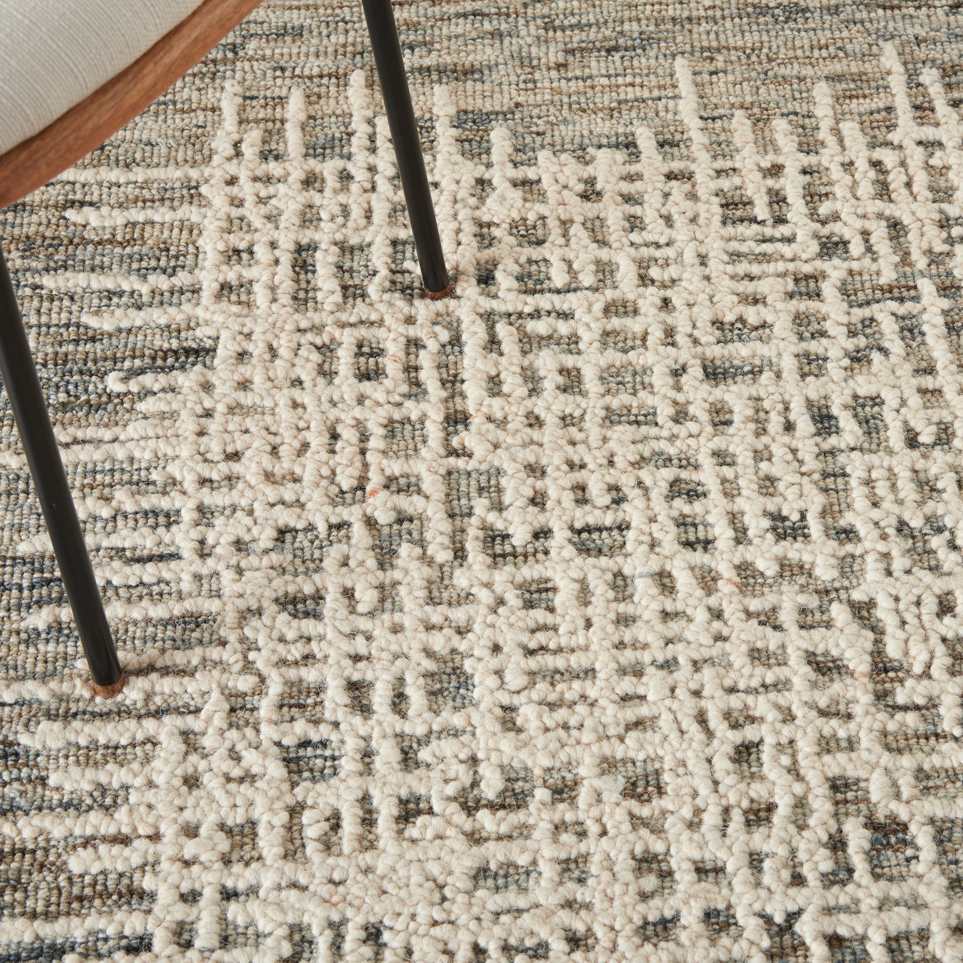 Close-up of a cream and gray patterned shag rug with chunky pile and black metal chair legs resting on it.