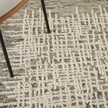 Close-up of a cream and gray patterned shag rug with chunky pile and black metal chair legs resting on it.