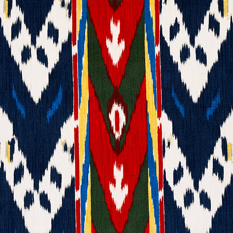 Ikat-inspired woven textile with navy blue and white geometric panels, a red central stripe with green diamonds, and yellow edging.