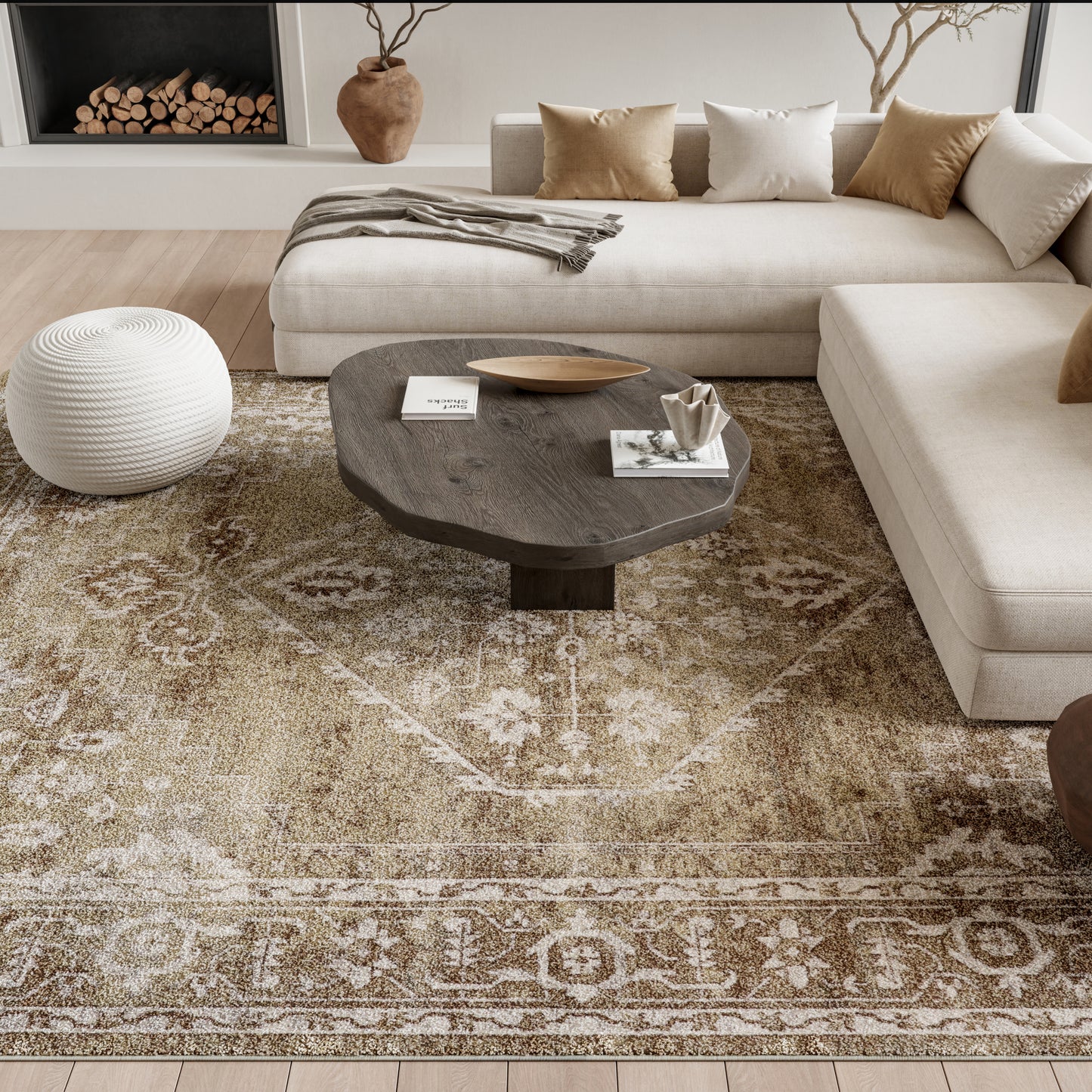 Vintage beige rug 7' x 9' on the floor in a living room, with a beige fabric sectional, tan and cream cushions, a dark wood round coffee table, and a white woven pouf.