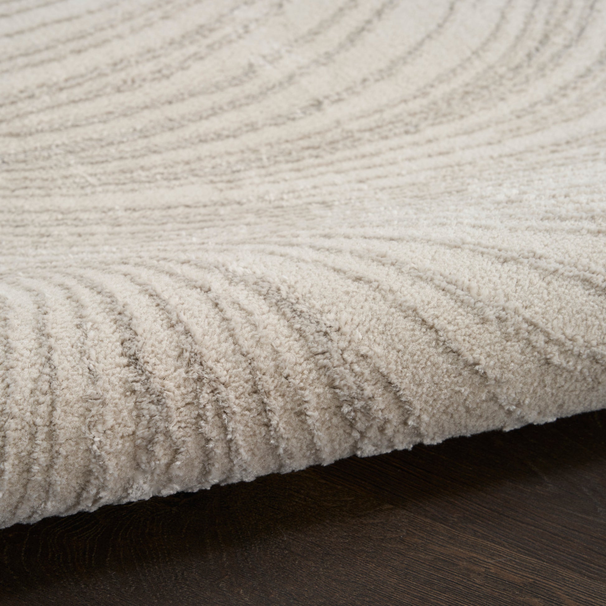 Beige textured pile area rug with concentric wave pattern on dark wood floor.