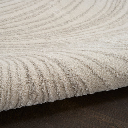 Beige textured pile area rug with concentric wave pattern on dark wood floor.
