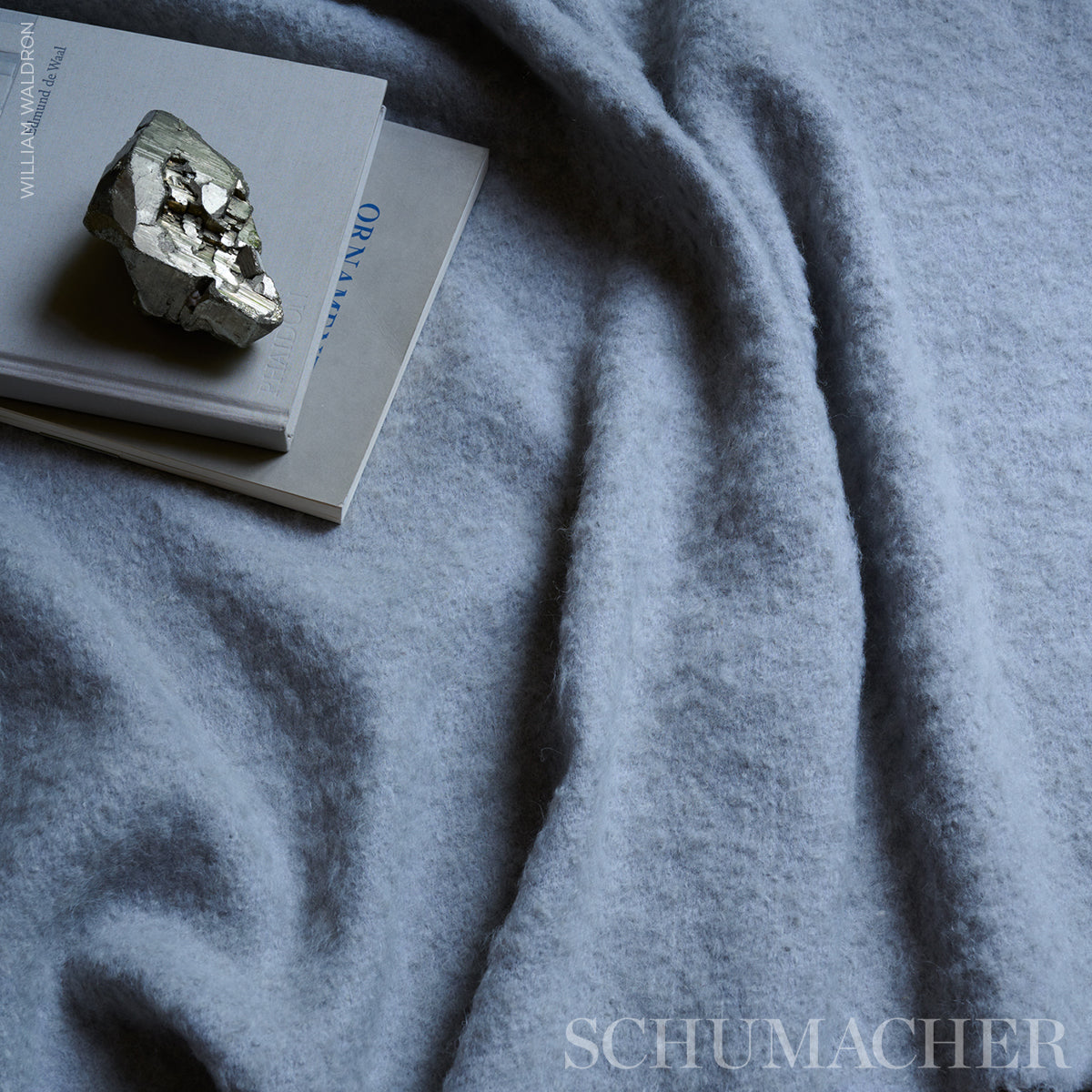 Blue-gray plush blanket draped over beige books with a metallic rock on top.