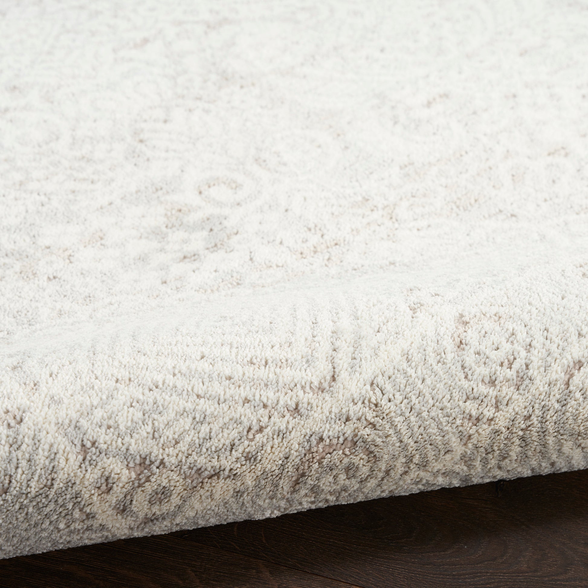 Cream textured area rug with subtle floral medallion pattern on dark wood floor.