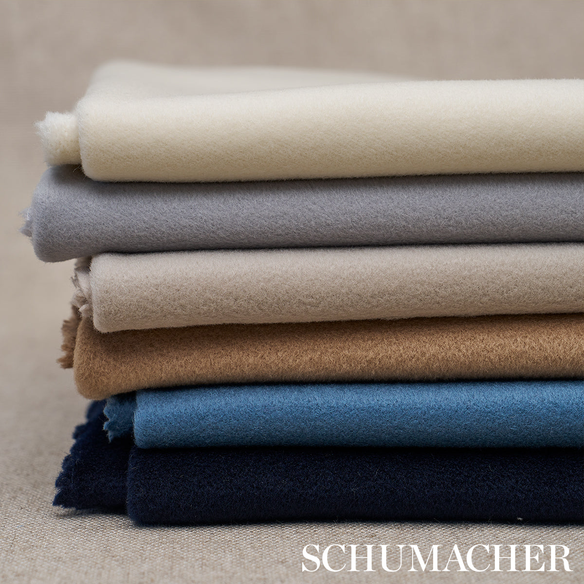 Stack of soft folded fleece blankets in cream, gray, beige, tan, blue, and navy; cozy throws.