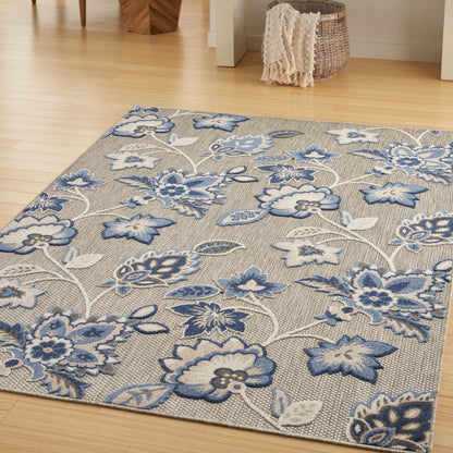 Rectangular rug with blue floral pattern on beige background, on light wood floor in a cozy room.