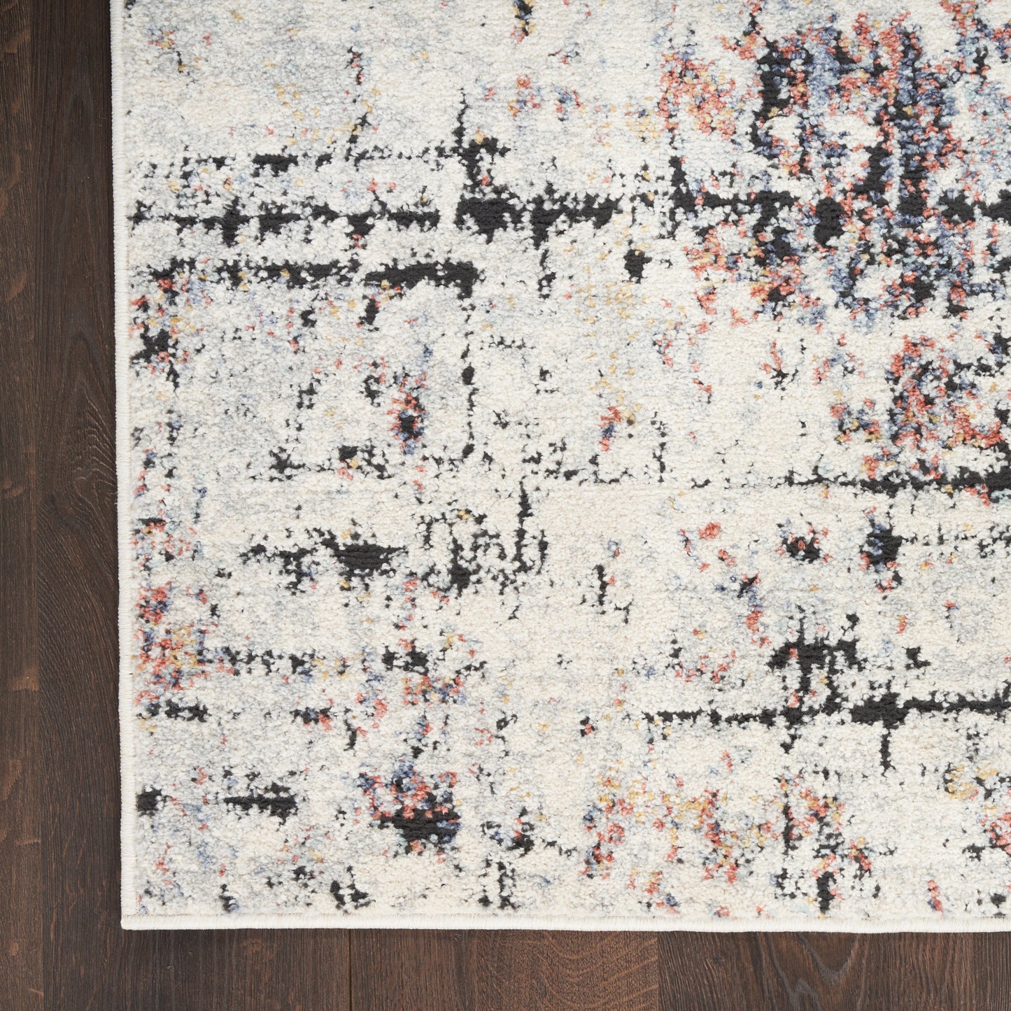 Abstract cream rug with black and multicolor specks on a dark wood floor; white edge binding.