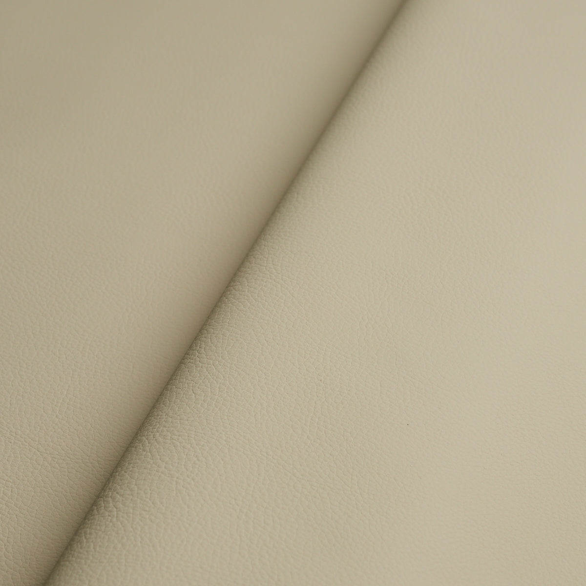 Beige faux leather with fine pebbled texture and a diagonal fold seam.