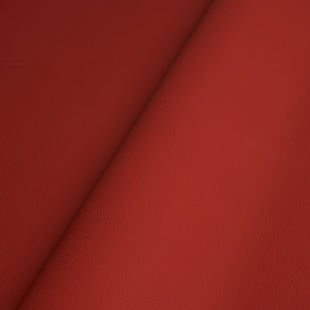 Close-up of red leather-textured material with visible grain and a diagonal fold.