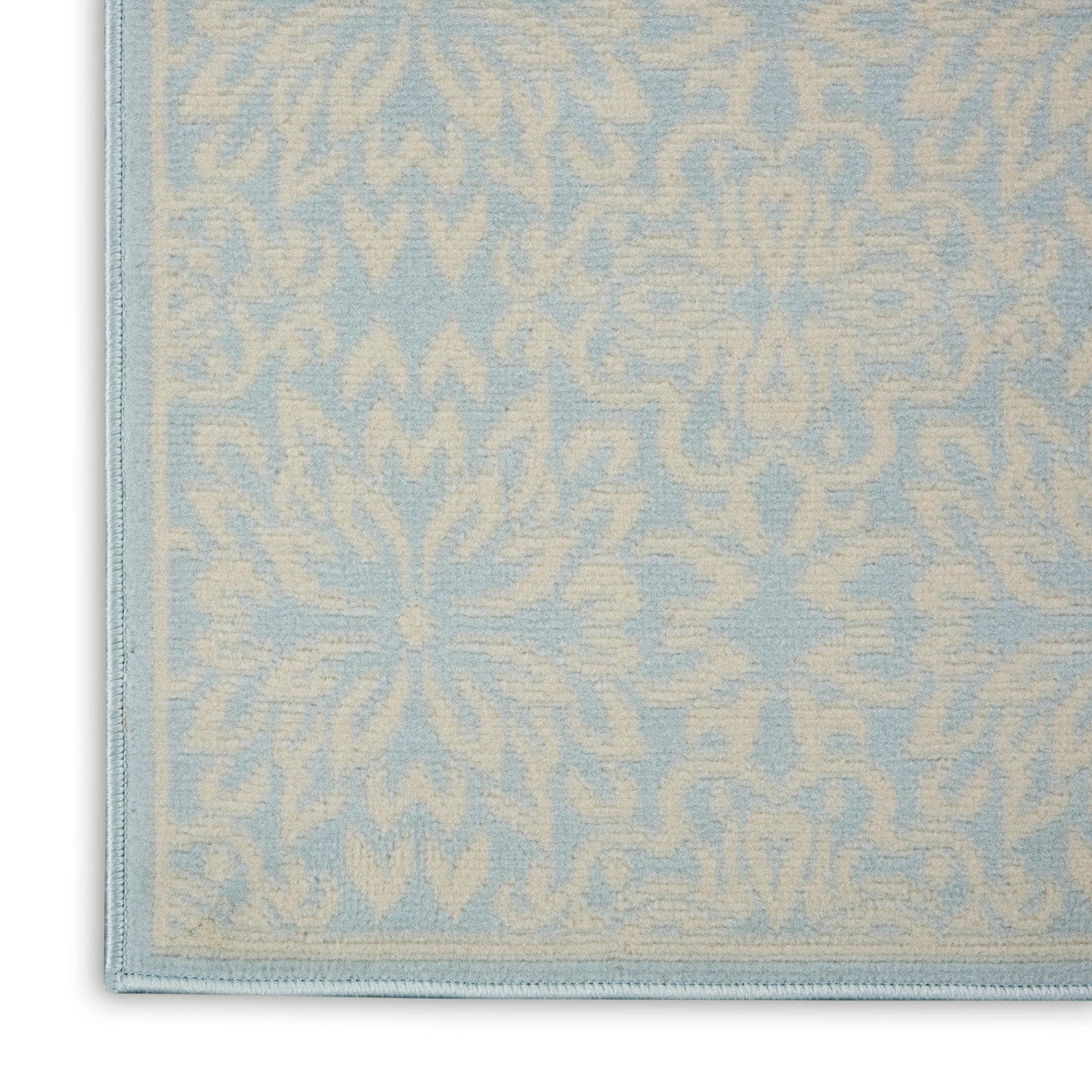 Light blue rug with cream damask floral pattern and stitched border, close-up corner view.