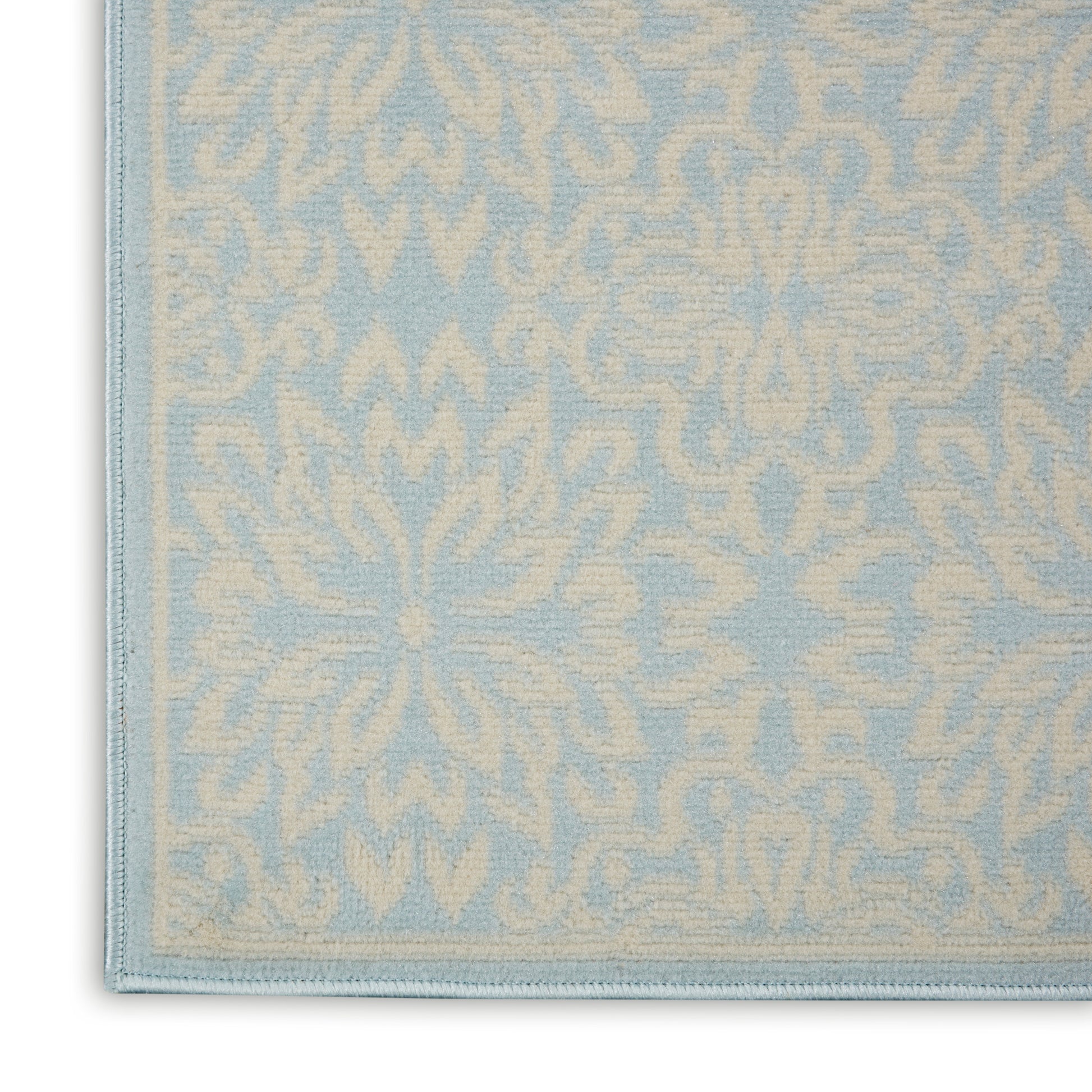 Light blue rug with cream damask floral pattern and stitched border, close-up corner view.