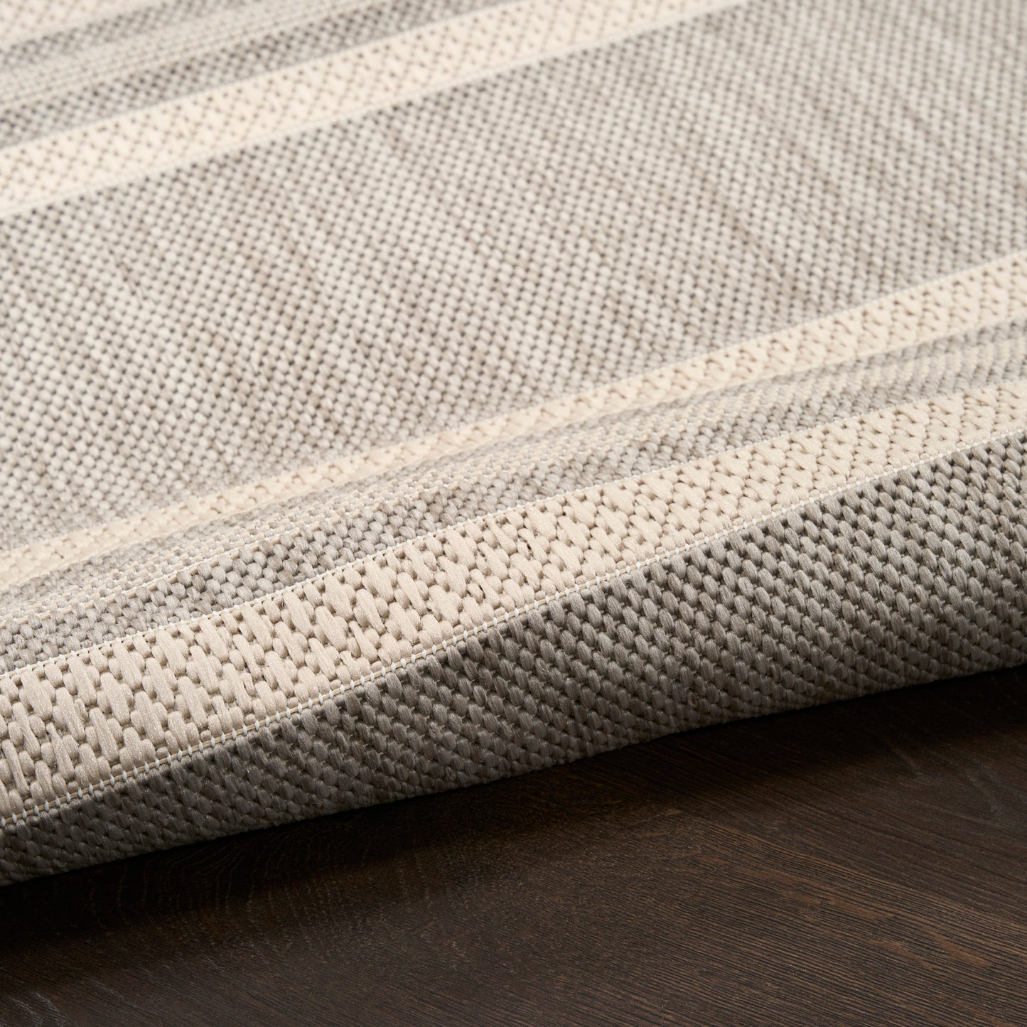 Beige & gray striped woven rug with folded edge on dark wood floor.