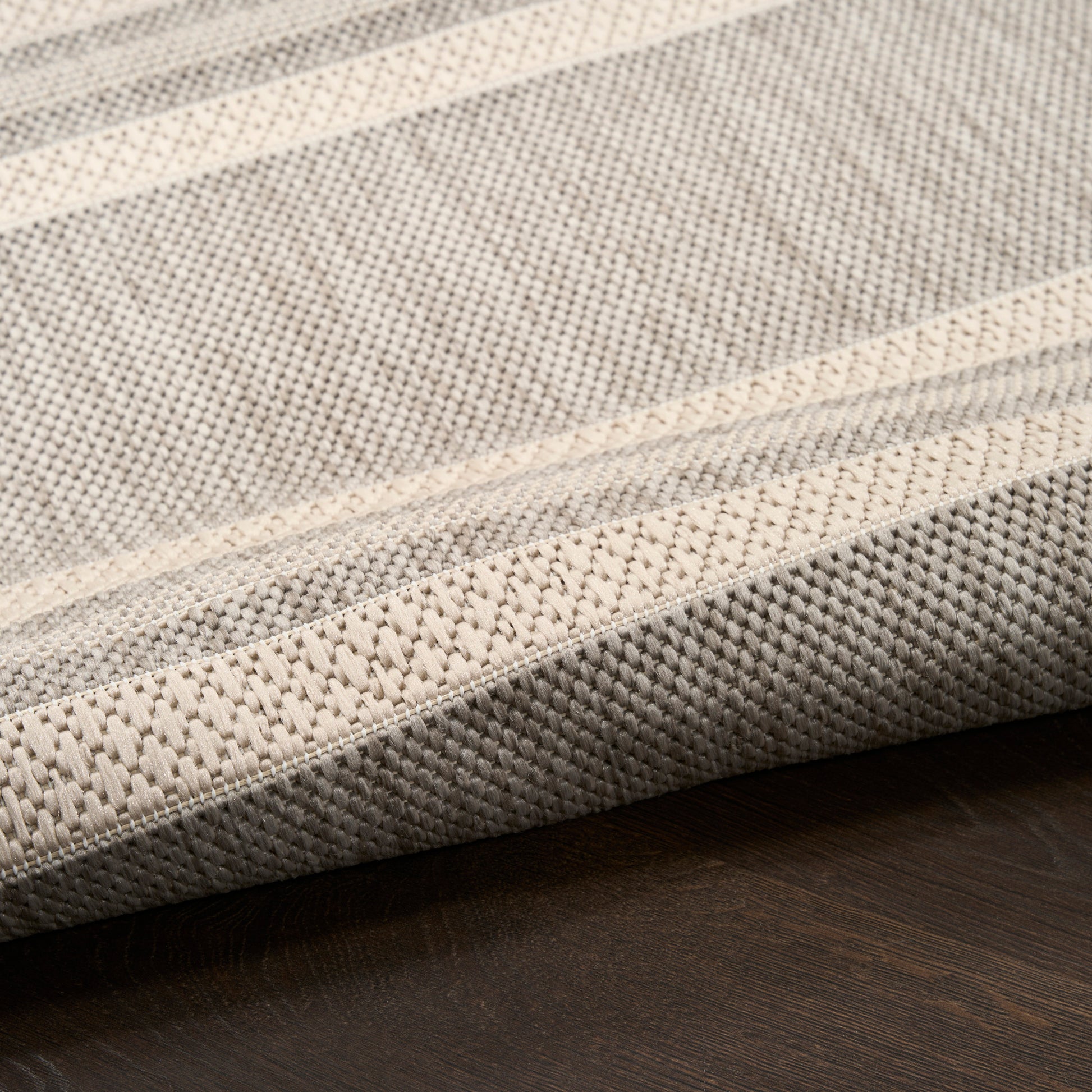 Beige & gray striped woven rug with folded edge on dark wood floor.