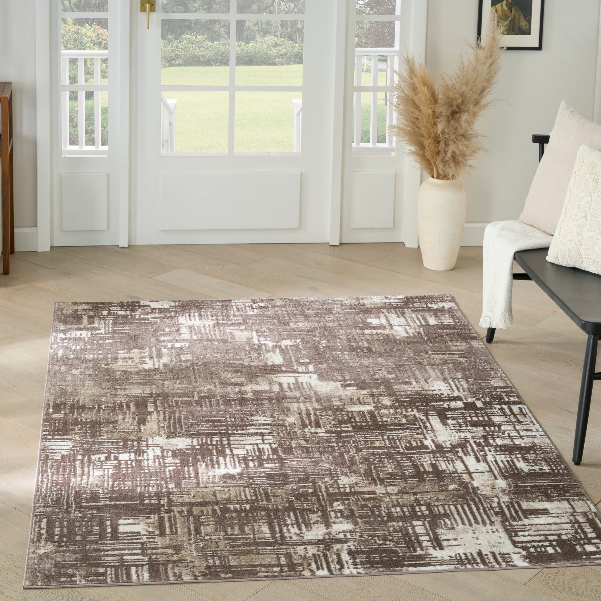 Taupe-brown abstract patterned area rug on light wood floor in a living room with pampas grass vase and neutral seating.