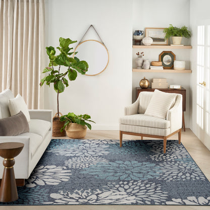 Neutral living room with beige curtains, white sofa, round hoop mirror, blue floral rug, and potted plants in woven baskets.