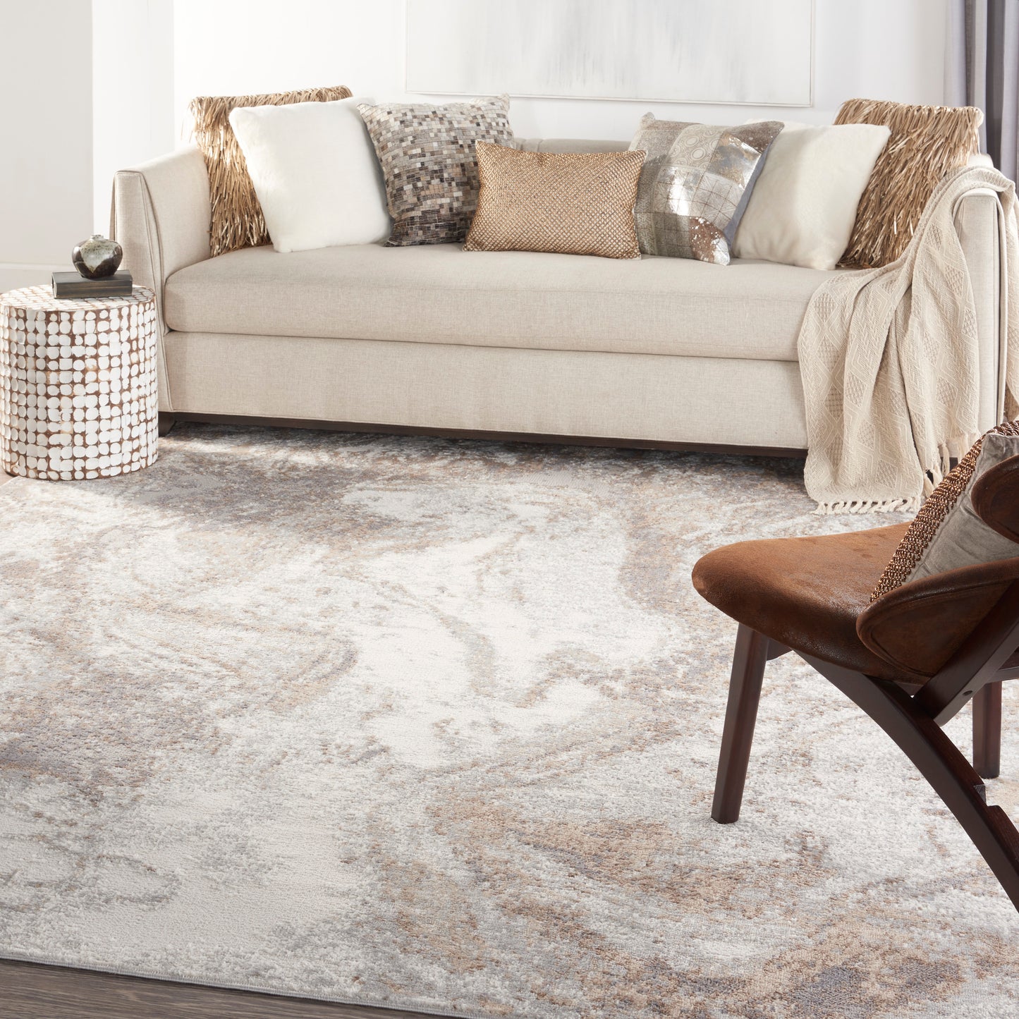 Beige patterned rug in a bright living room, with a mosaic side table, brown armchair, and a beige sofa with assorted pillows and a throw.