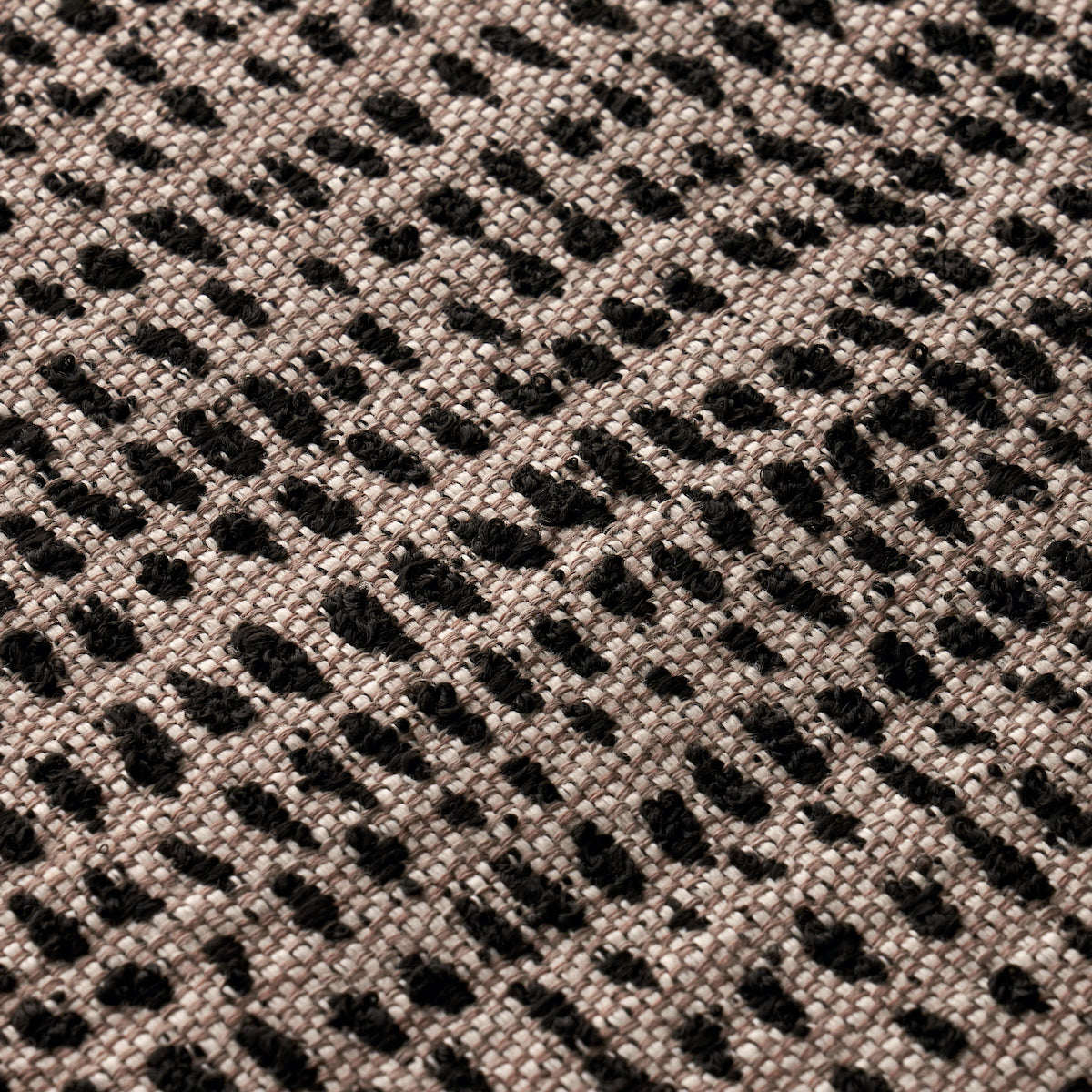 Beige woven fabric with irregular black dot pattern and textured surface.
