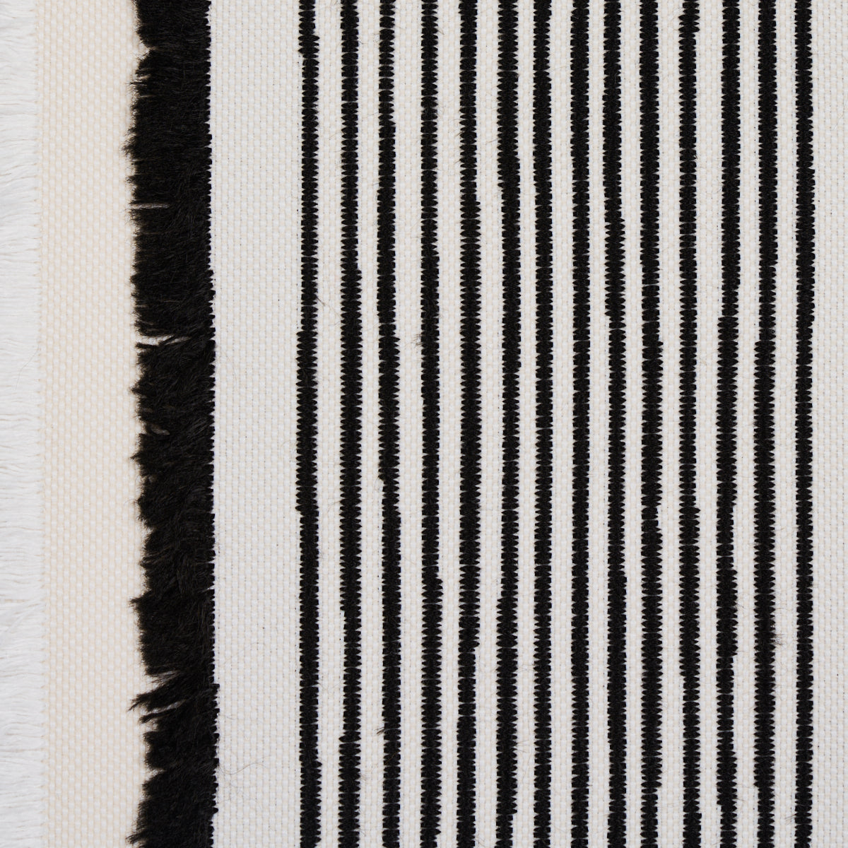 Close-up of a black-and-white striped woven textile with a fringe edge; vertical narrow stripes on a light backdrop.