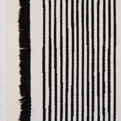 Close-up of a black-and-white striped woven textile with a fringe edge; vertical narrow stripes on a light backdrop.