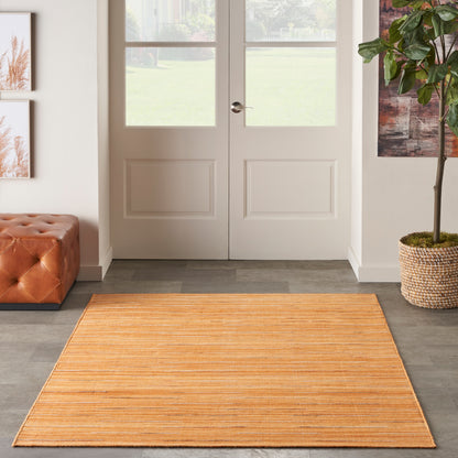 Orange rectangular striped rug in entryway with white double doors, tufted leather ottoman on left and potted plant on right.
