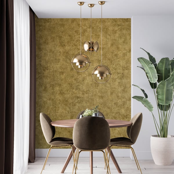 Gold textured wallcovering with a subtle cord pattern on the wall behind a dining room setup: round wooden table, brown upholstered chairs with gold legs, two globe pendant lights, and a plant.