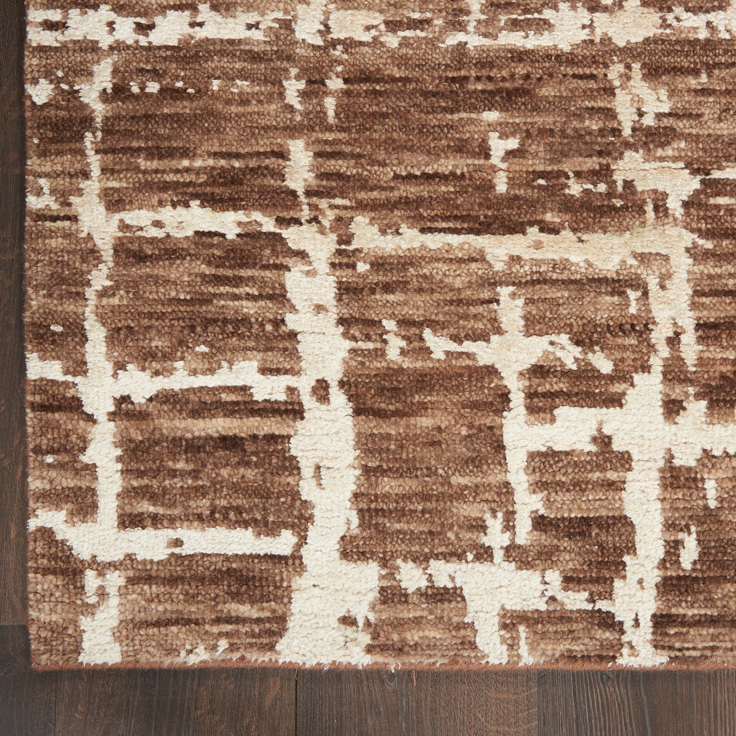 Brown and cream geometric patterned rug with textured pile on dark wood floor.