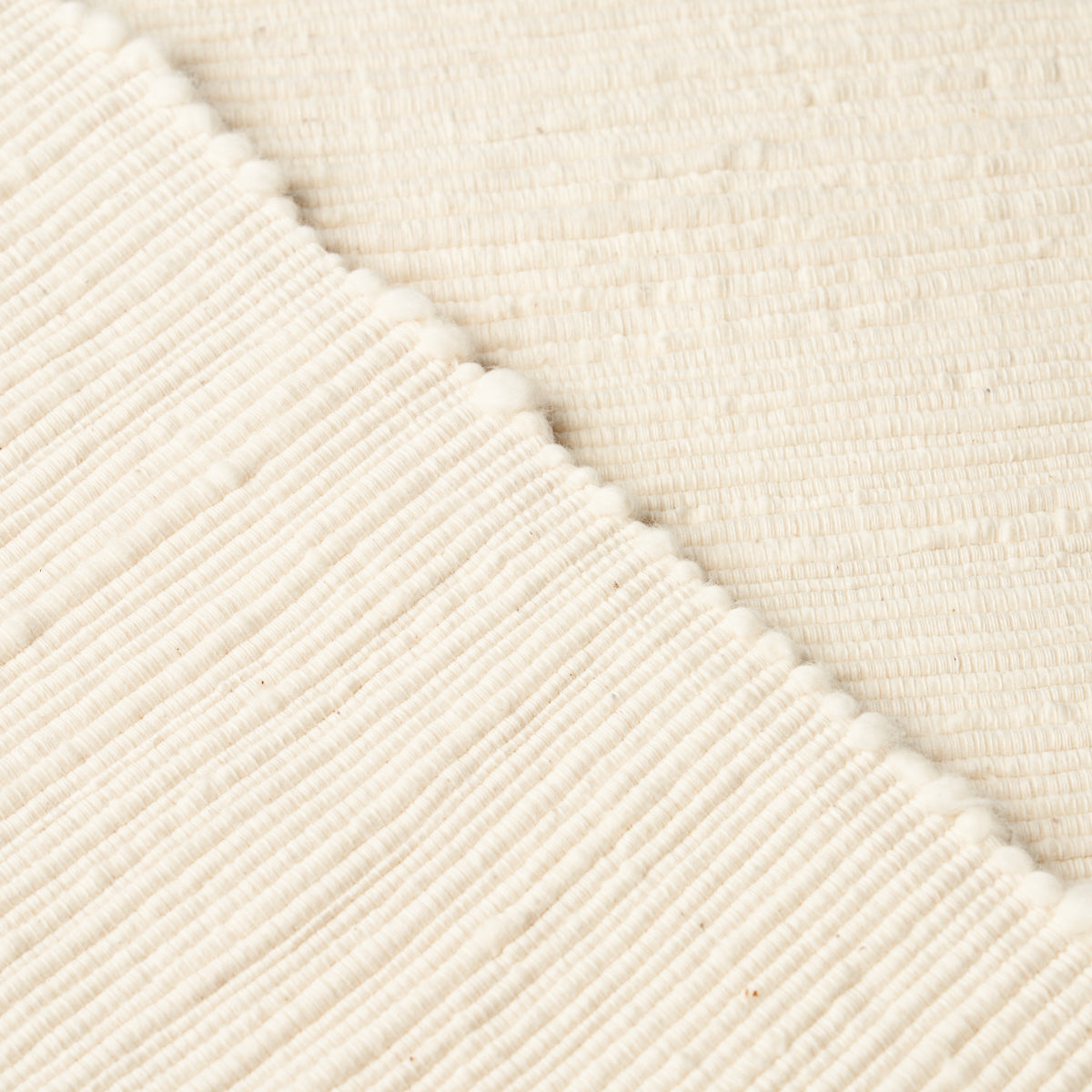 Cream knitted fabric with ribbed texture and tiny pom-pom trim along diagonal seam; cozy throw blanket.