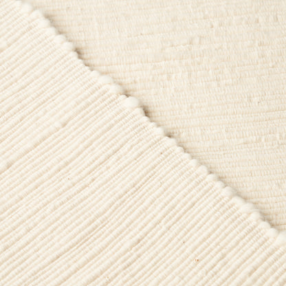 Cream knitted fabric with ribbed texture and tiny pom-pom trim along diagonal seam; cozy throw blanket.