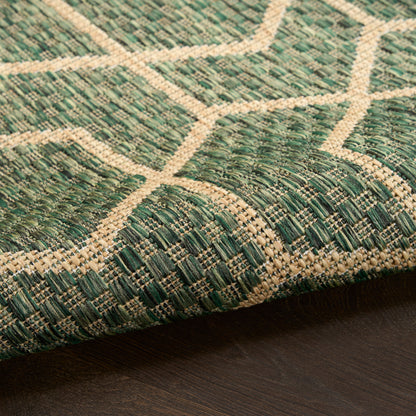 Close-up of green woven rug with beige lattice pattern on dark wooden floor.