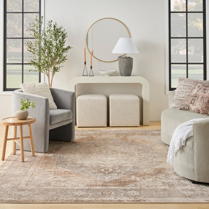 Neutral living room with gray seating, beige rug, round wall mirror, console table, two ottomans, plant, lamp.