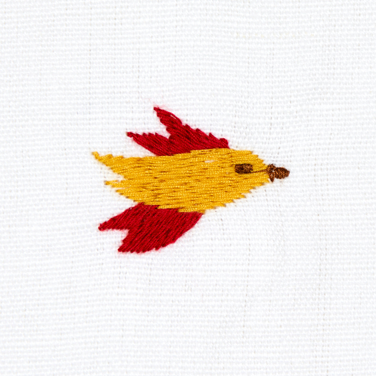 Embroidered yellow fish with red fins on white fabric.
