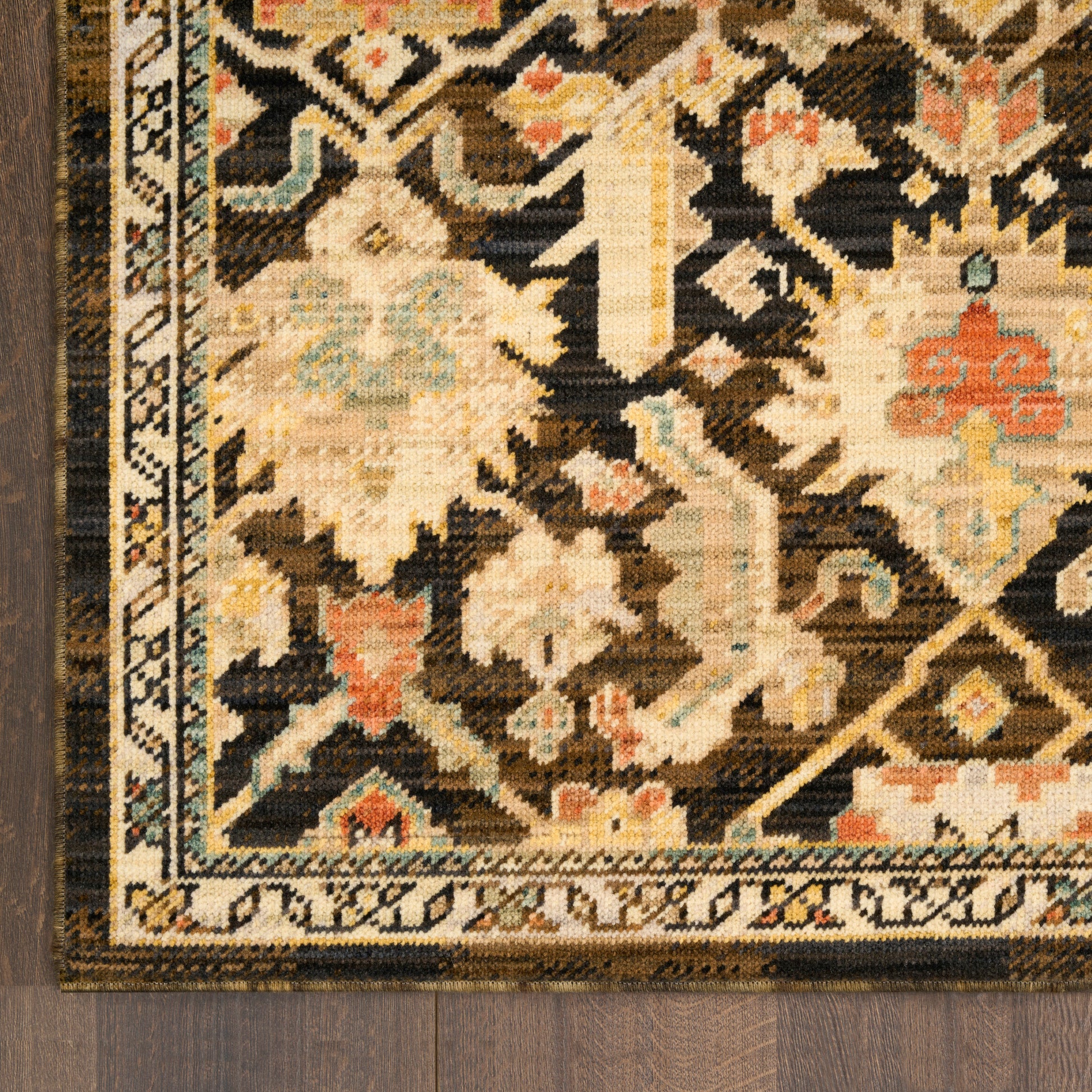 Close-up of an oriental rug with cream, tan and black, featuring floral motifs and a bordered geometric pattern on dark wood.