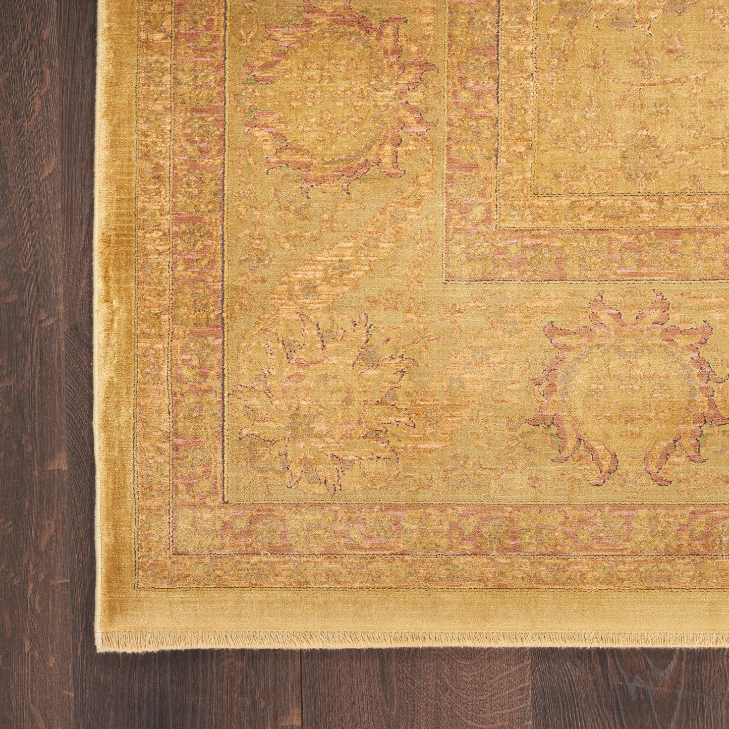 Golden Oriental area rug with pink border, floral medallions, fringed edge, on dark hardwood floor.