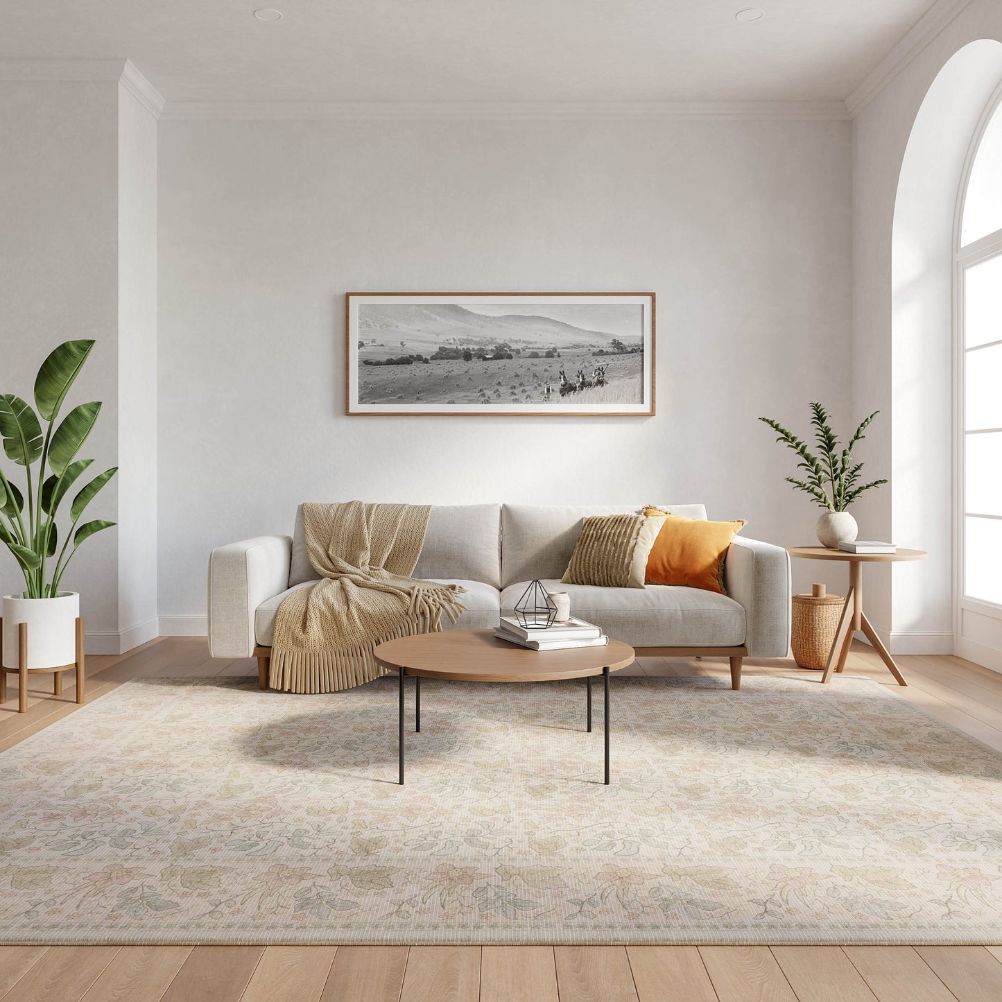 Light gray rug (8' x 10') in a living room setting with a sofa, beige throw, orange cushion, round wood coffee table, framed landscape art, plants, and an arched window.