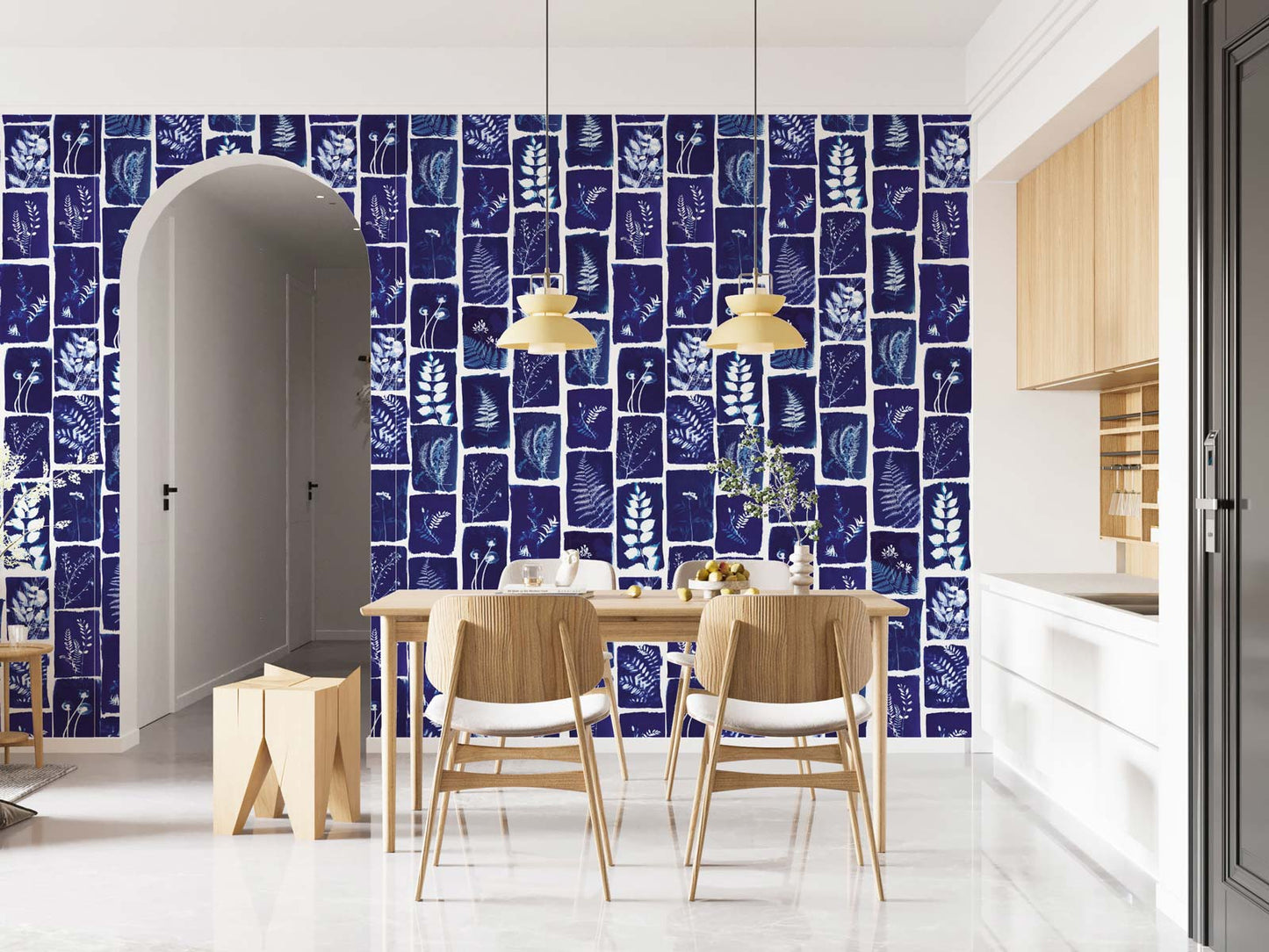 Dining area featuring navy botanical-pattern wall mural, with light wood table and chairs, pendant lights, arch doorway and white kitchen.