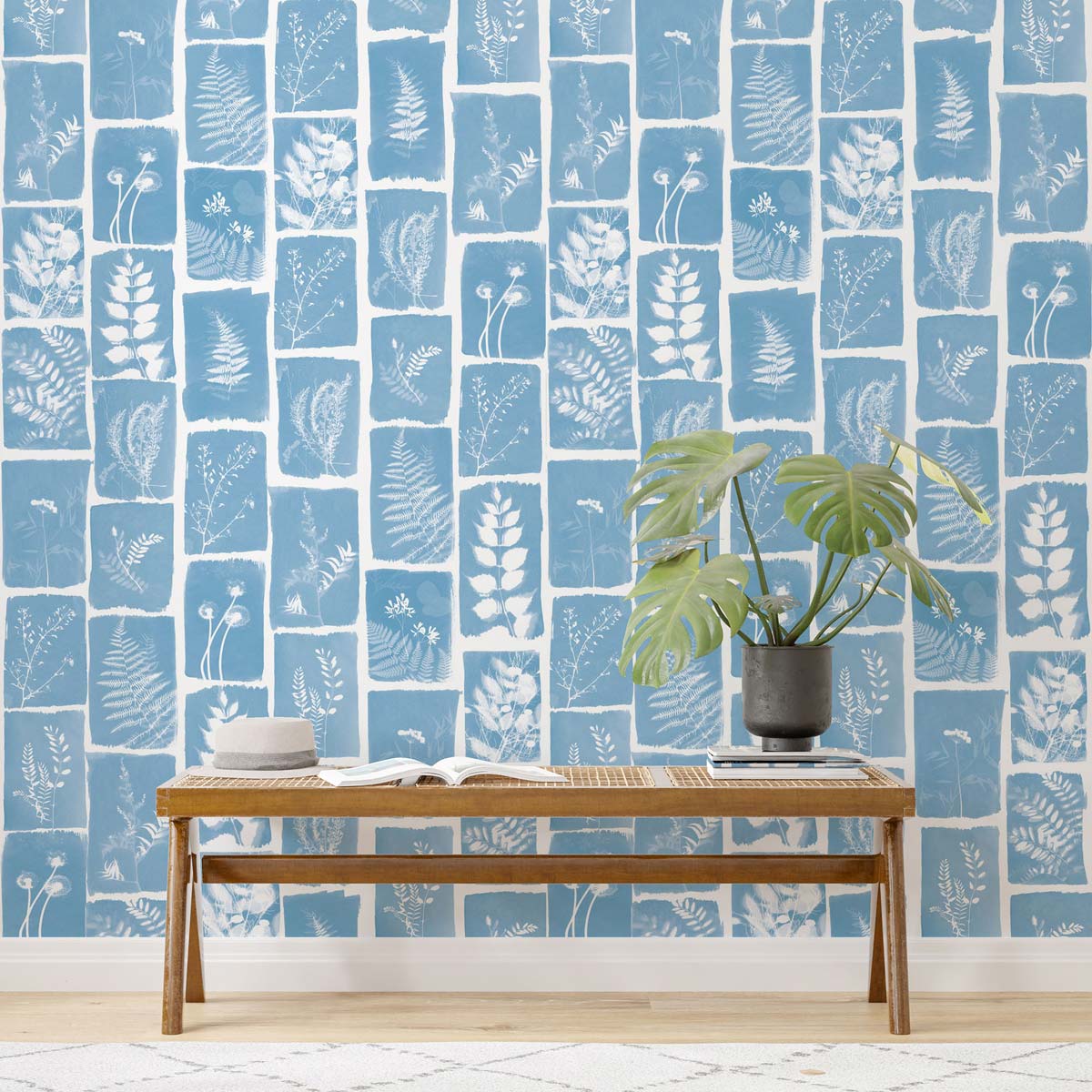 Blue botanical wall mural with white leaf prints in tile panels; wooden bench with a potted plant and a book.
