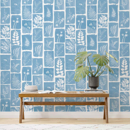 Blue botanical wall mural with white leaf prints in tile panels; wooden bench with a potted plant and a book.