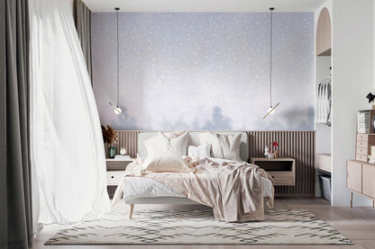 Cozy bedroom scene with beige bed, blush throw, white bedding, white nature wall mural with starry accents, wooden slatted headboard, pendant lights.