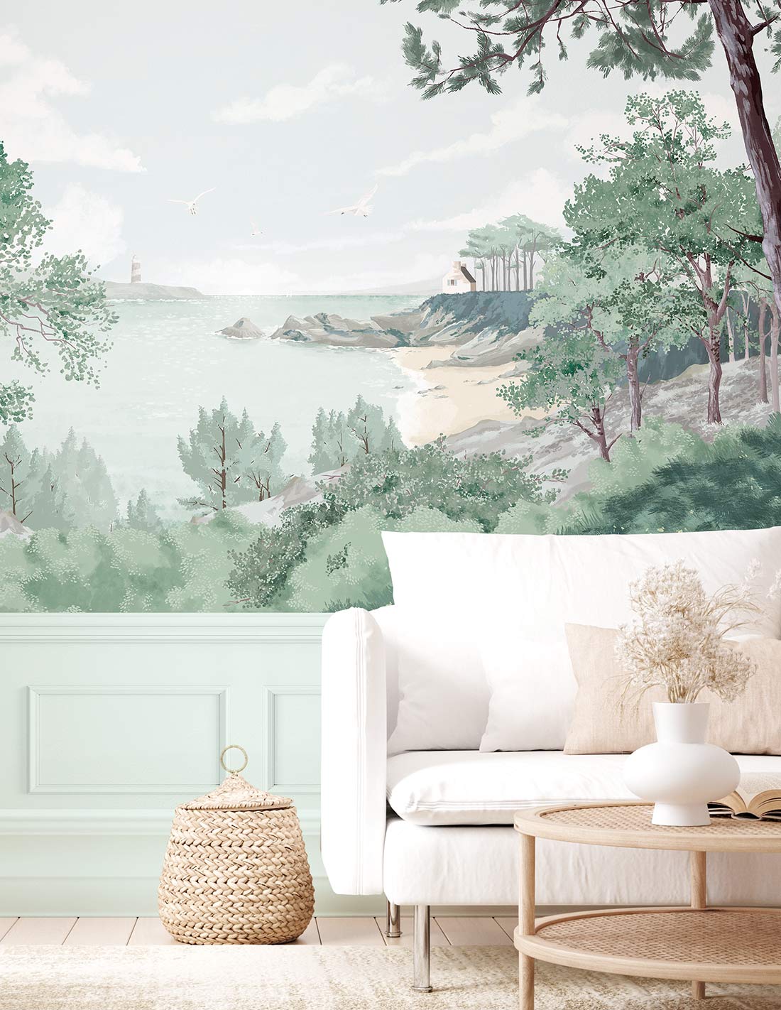 Pastel coastal living room with ocean and cliff mural, mint wainscoting, white sofa, round wooden coffee table, woven basket.