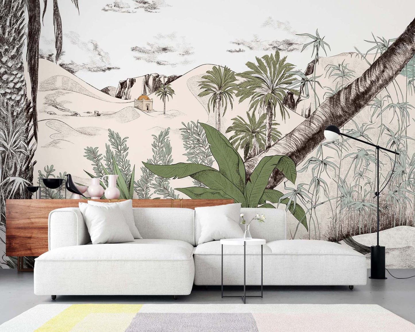 Light gray sectional sofa with white cushions in front of a green landscape wall mural with palm trees; wooden console, black arc lamp, pastel rug.
