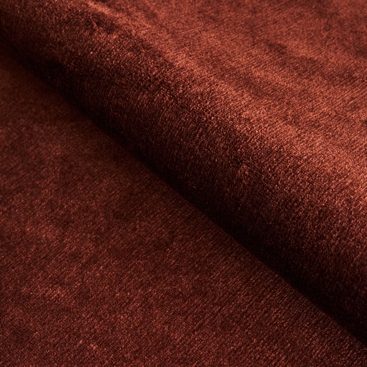Rust-red velvet fabric close-up with soft pile and folded drape.