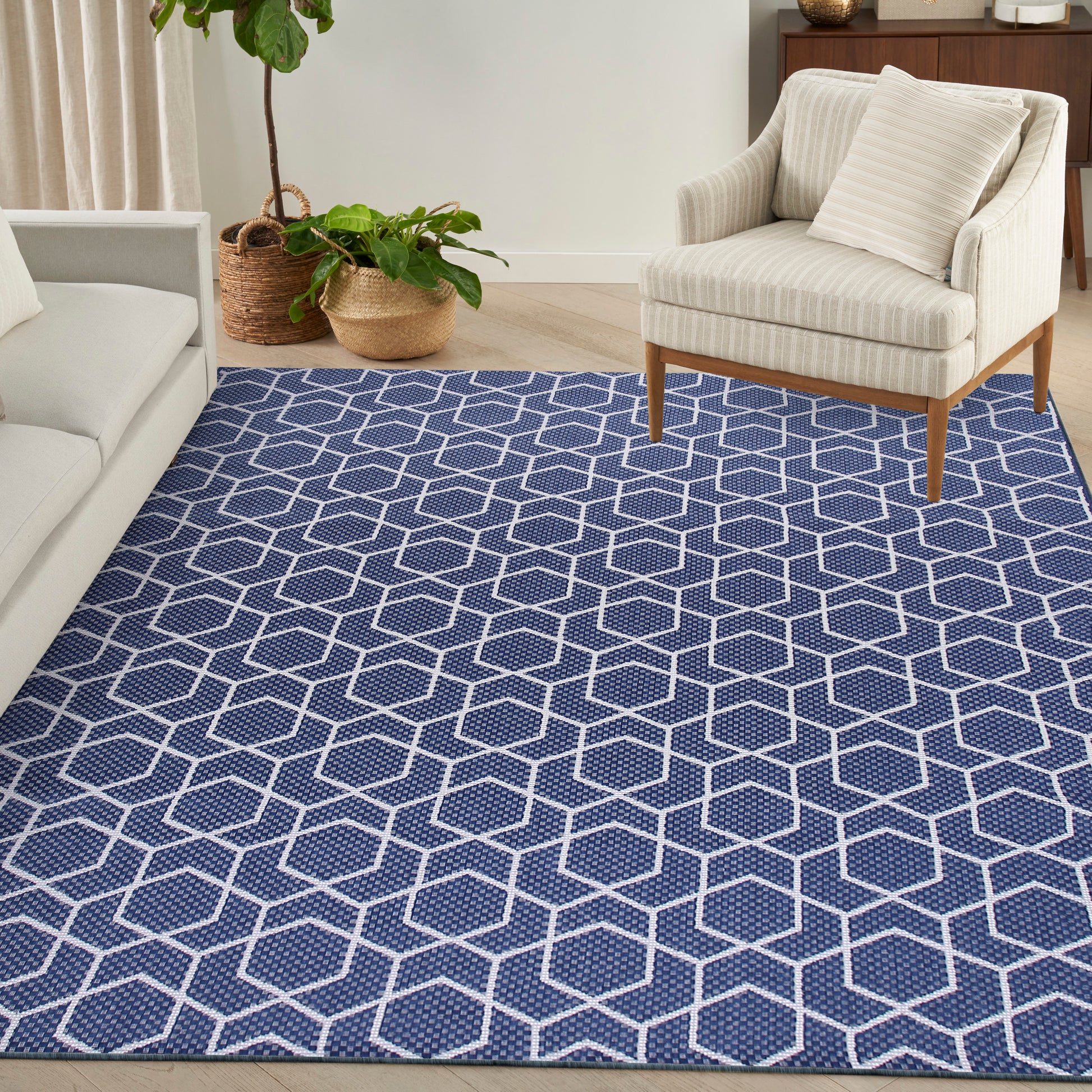 Navy blue rug with white hexagon lattice in a modern living room, cream sofa, striped armchair, and potted plants.