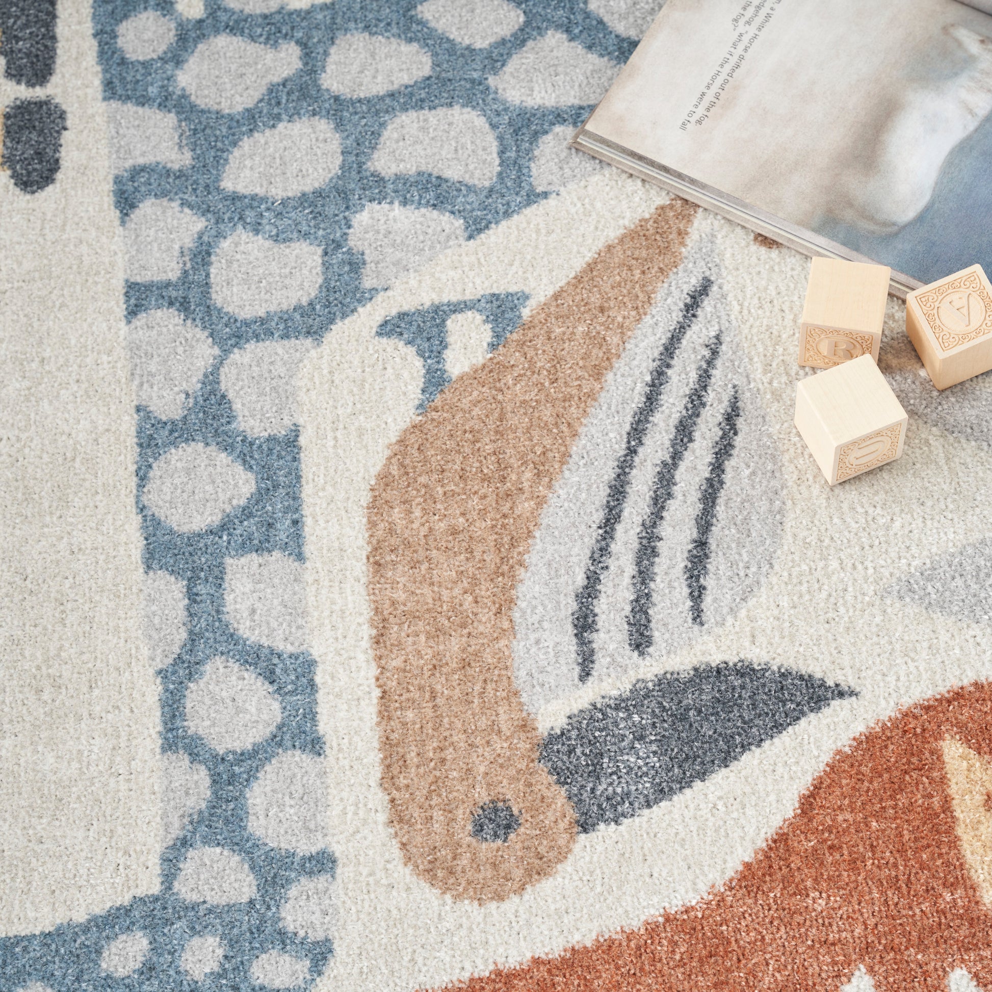 Soft, shaggy abstract-pattern area rug in blue, beige and orange with wooden blocks and an open magazine.