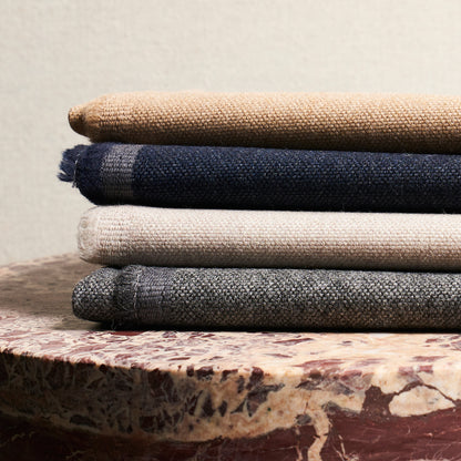 Stack of folded textured fabrics in beige, navy, taupe and gray on a marble table.