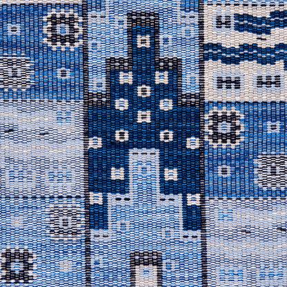 Close-up of blue woven fabric with a navy central cross motif, white dot accents, and light-blue panels.