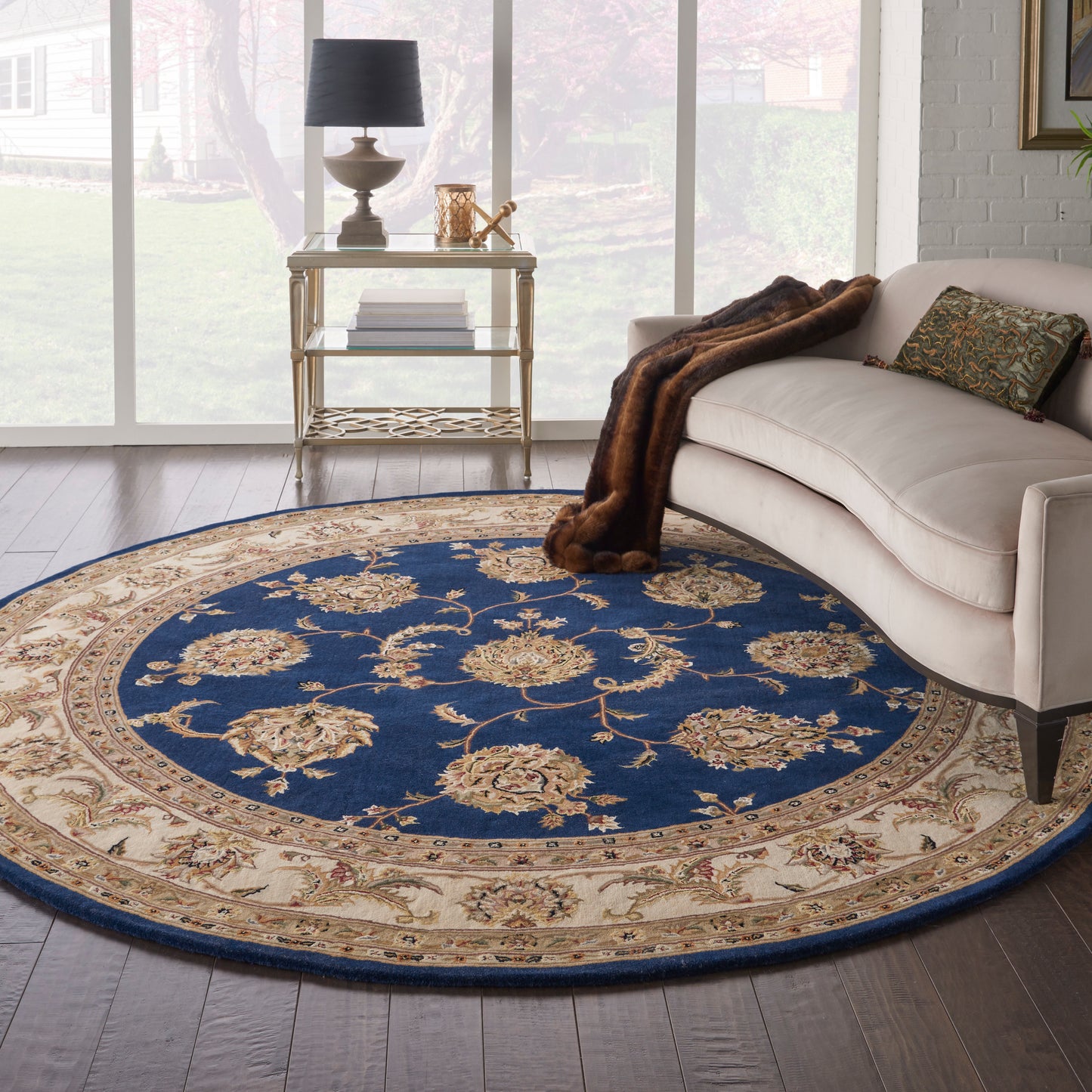Round blue and beige floral rug under a cream sofa with a fur throw and gold side table.