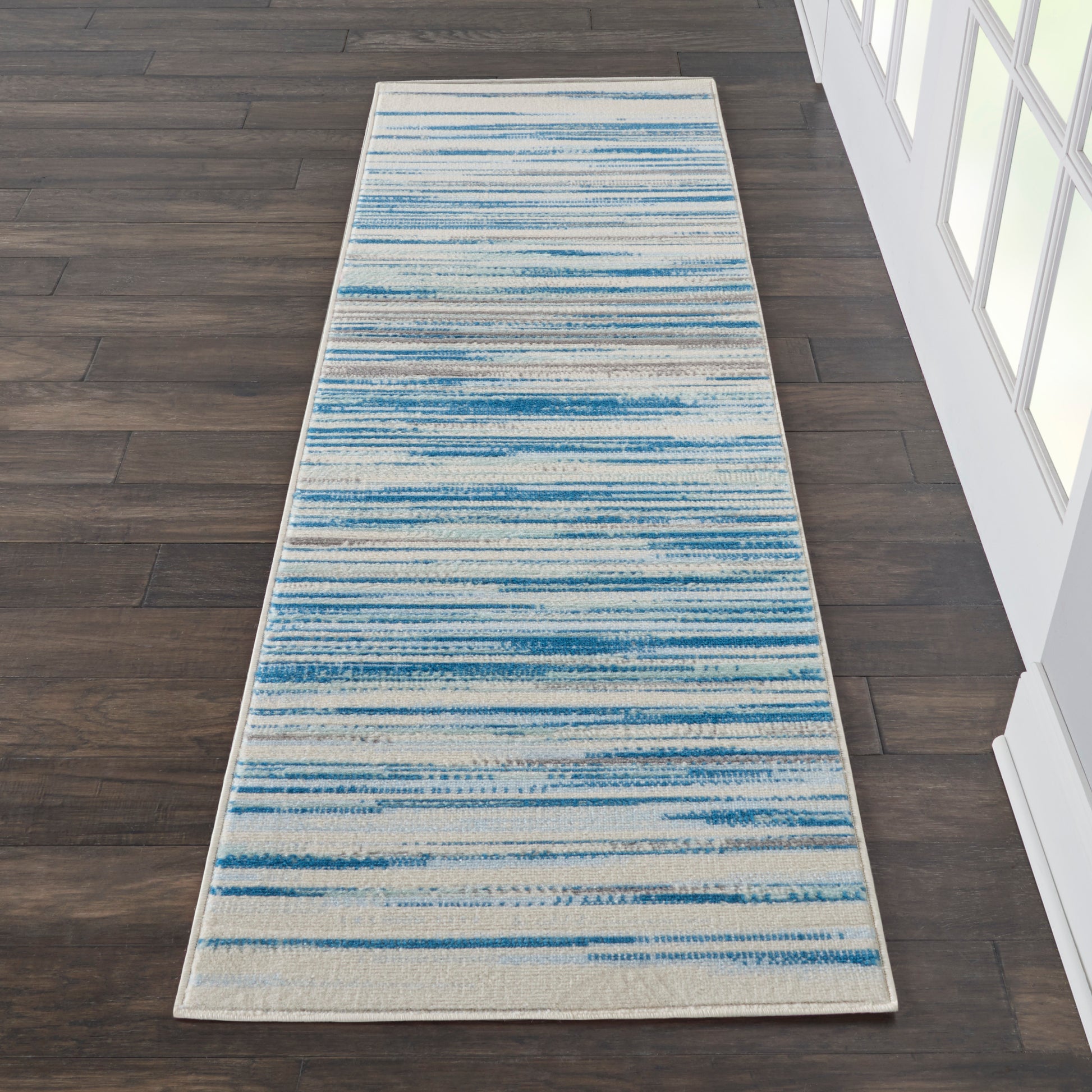 Rectangular rug runner with varying blue brushstroke stripes on cream background, modern hallway/entryway decor.