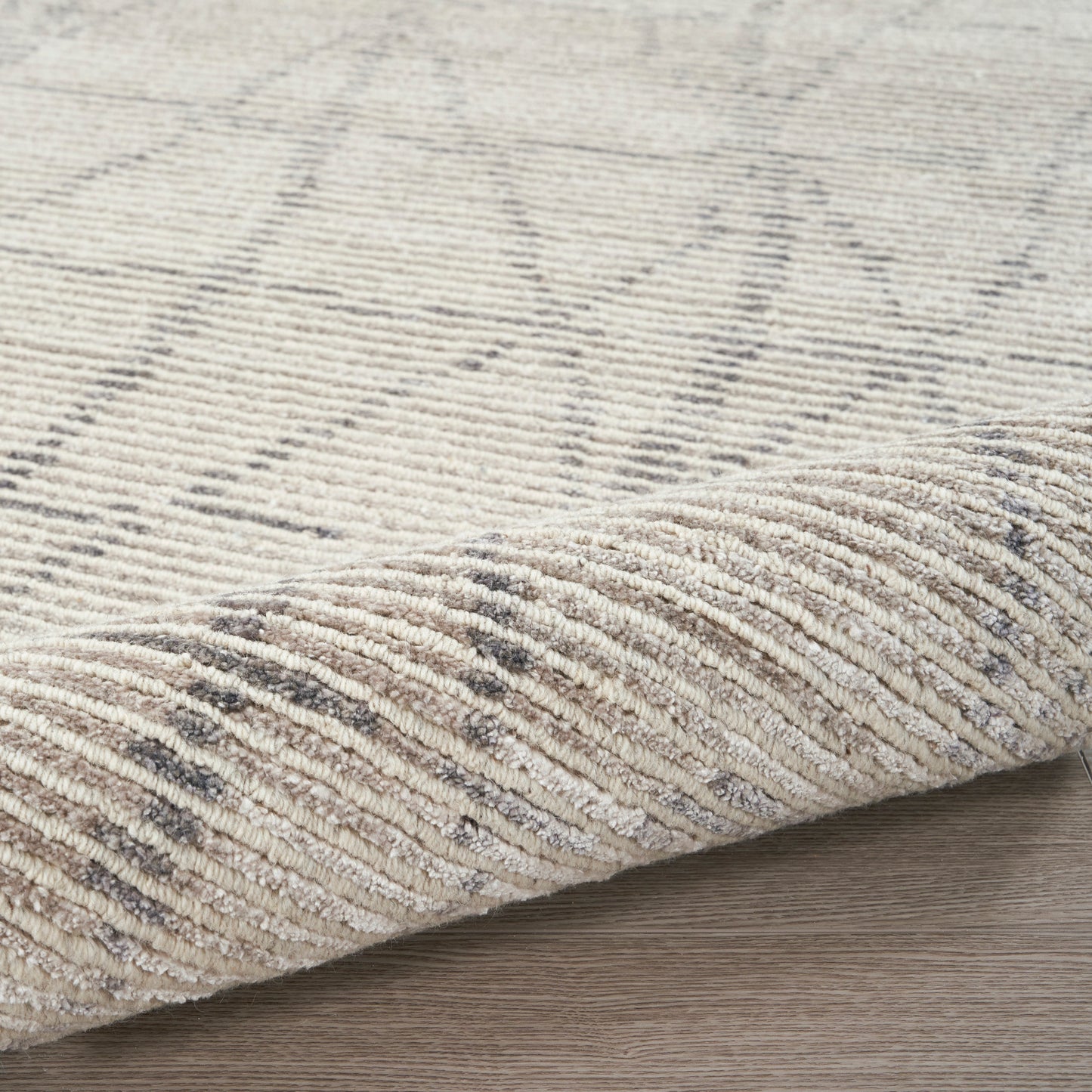 Beige textured area rug with subtle grey geometric pattern, folded edge on light wood floor.