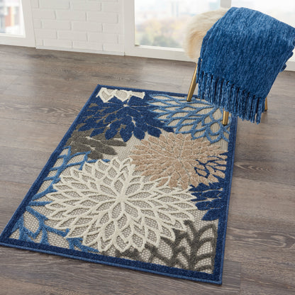 Blue-fringe area rug with large white and beige floral pattern on a dark blue border, on wooden floor beside a blue throw.